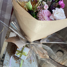 Load image into Gallery viewer, A bouquet of mixed flowers wrapped in beige kraft paper and clear cellophane, tied with a ribbon, placed on a rustic wooden surface next to a small gift box. includes a luxury tropic skincare body pebble soap gift bundle