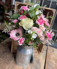 Load image into Gallery viewer, pink and cream flowers presented in a metal milk churn from bits and buds luxury florist in Leighton Buzzard. Displayed on a rustic wooden bench bathed in sunlight.

