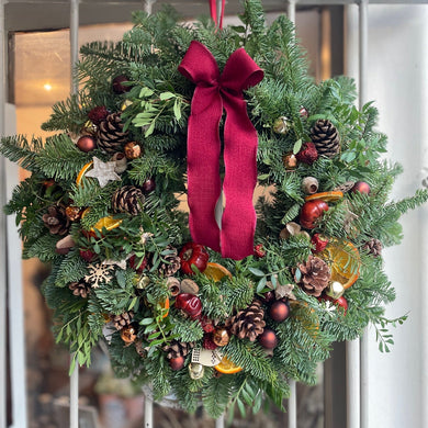 Christmas wreath with red ribbon hanging on a door natural decorations with pine cones and brown copper baubles