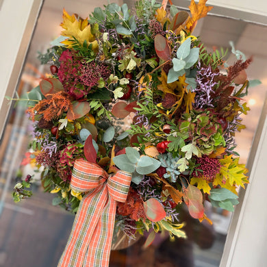 A wreath of various dried flowers and foliage in shades of autumn, displayed in front of a dark background.