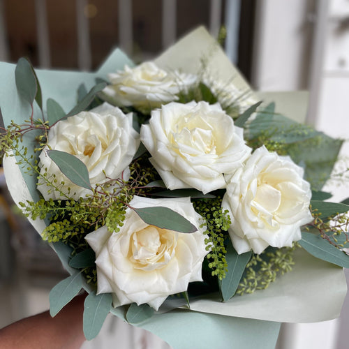 Bouquet of white roses with greenery held by a person indoors. made at bits and buds florist leighton buzzard.