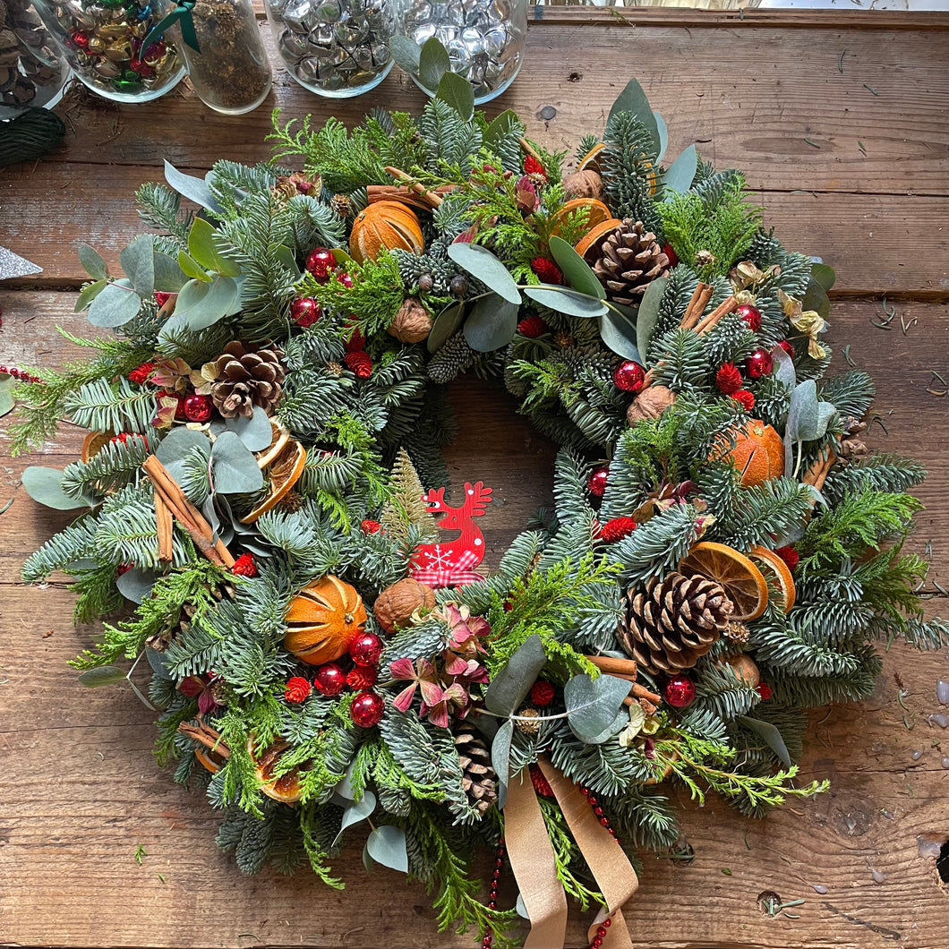 A Christmas wreath with green foliage, red berries, brown pine cones, and a decorative element shaped like a reindeer peeking out.