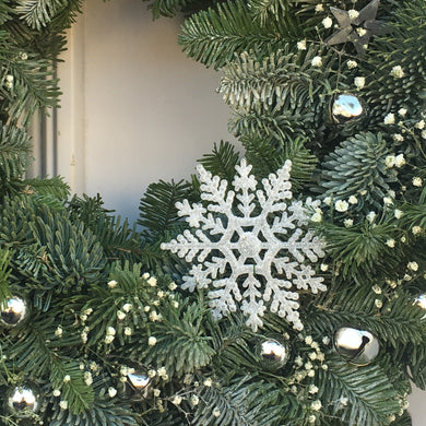 a white and silver door wreath with jingle bells and fresh flowers on a wreath of spruce and blue pine